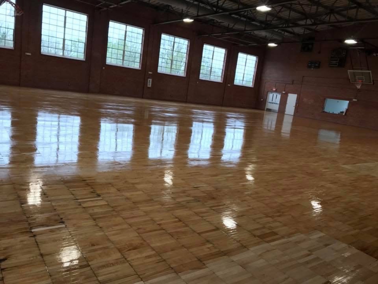 A full gymnasium floor, sanded and refinished, light pouring through tall windows